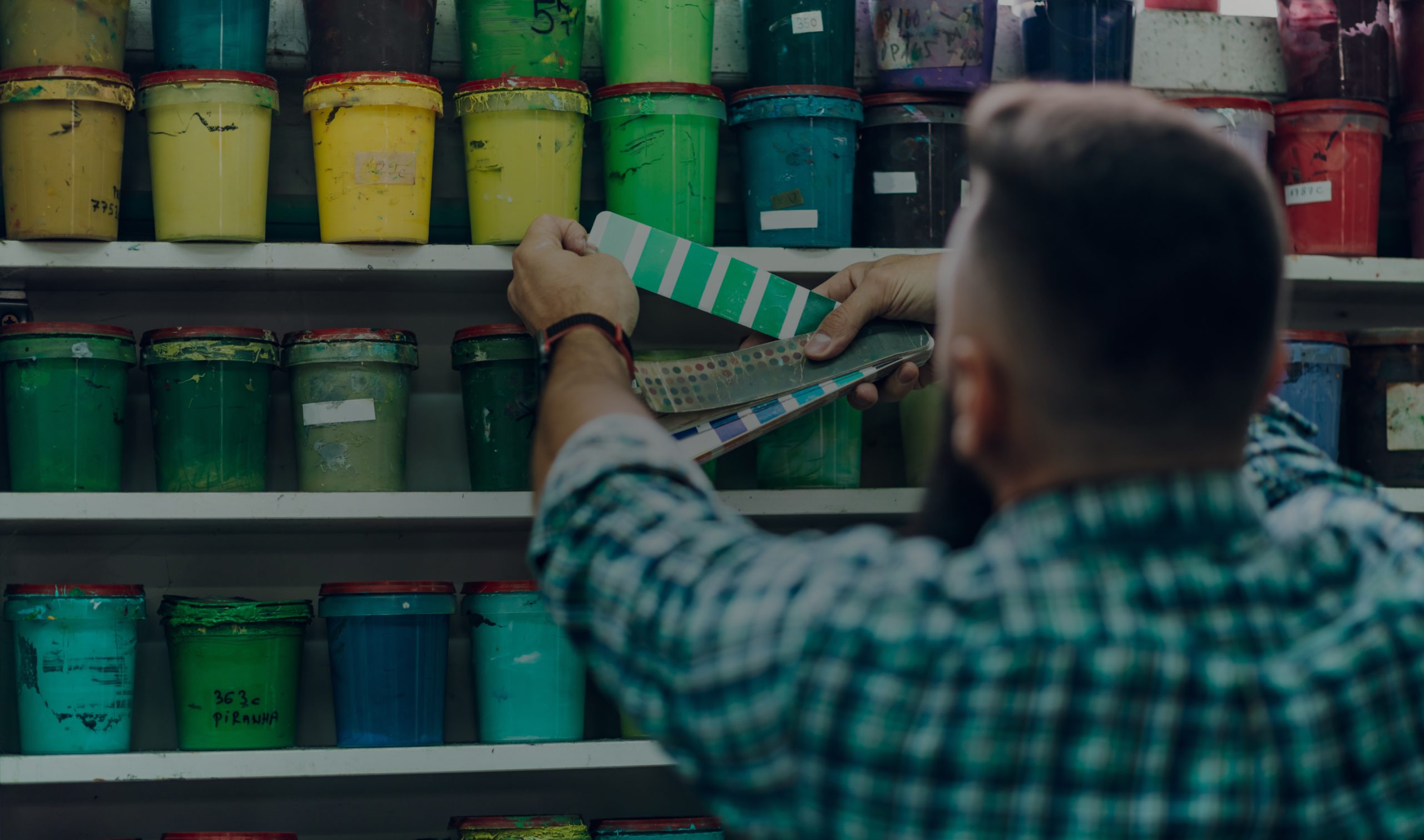 A pressman comparing color swatches with ink buckets on the shelf